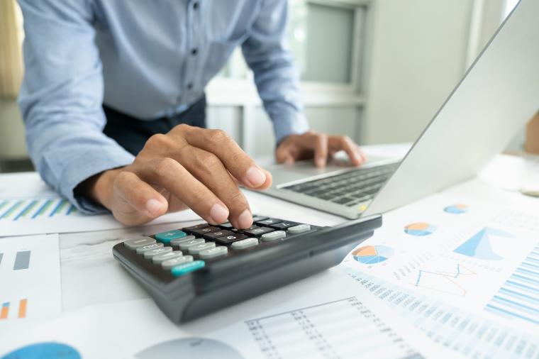 person using calculator among spreadsheets and laptop