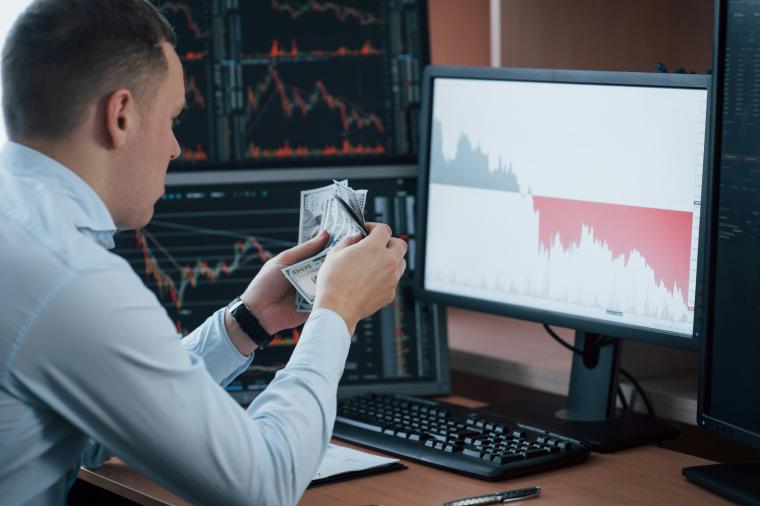 man counting currency in front of computer