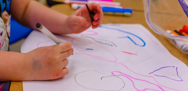 child coloring, hands with crayons over paper