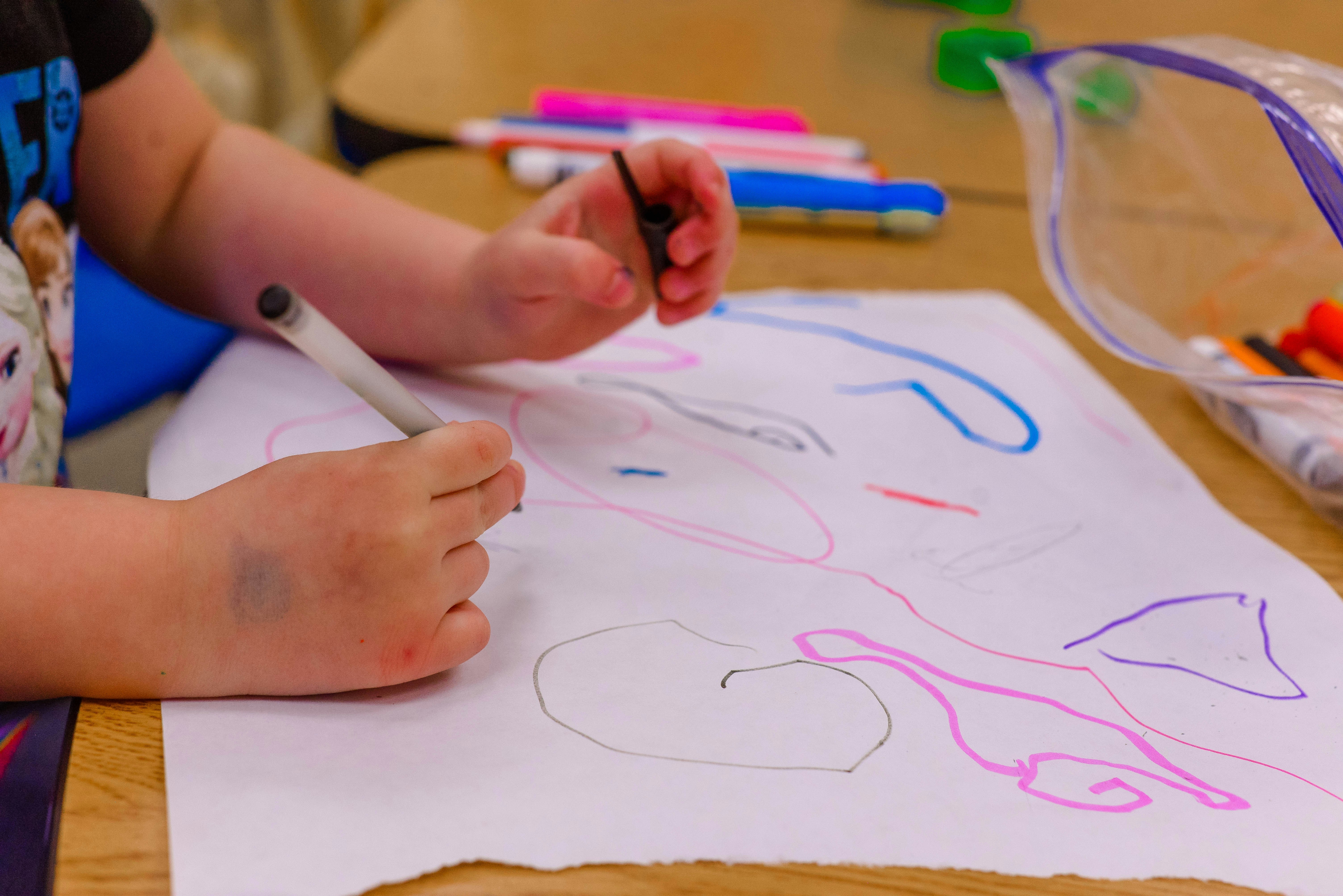 child coloring, hands with crayons over paper